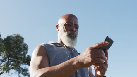 hombre afroamericano de alto nivel haciendo ejercicio usando un teléfono inteligente poniendo auriculares