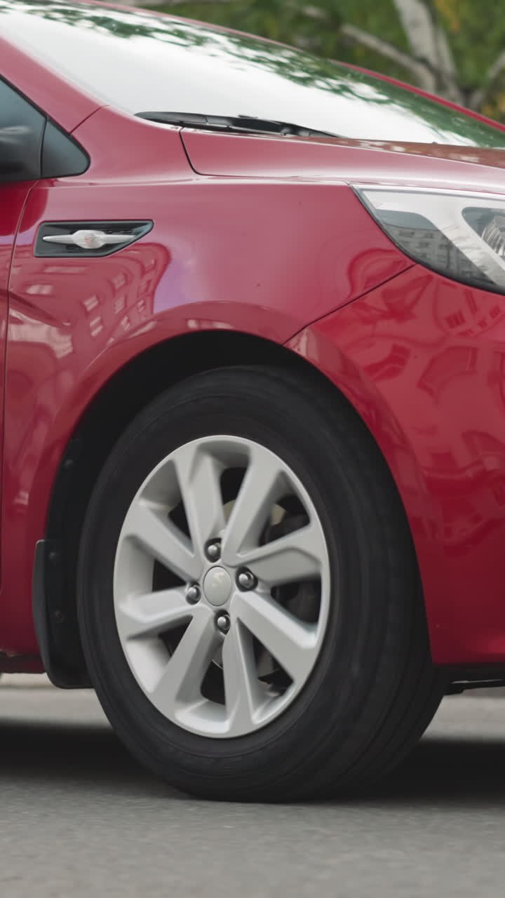 Elegant red car drives on asphalt road in center of city on summer day. Modern sedan vehicle in downtown. Automobile moves on street closeup
