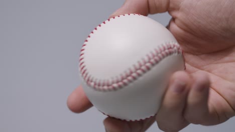 close up shot of hand holding baseball ball against grey background 1