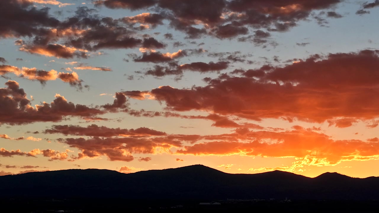 Timelapse 4K con dron de un clima cambiante del suroeste al atardecer. Luz radiante ilumina formaciones de nubes sobre una silueta oscura de montaña en el paisaje accidentado del desierto alto