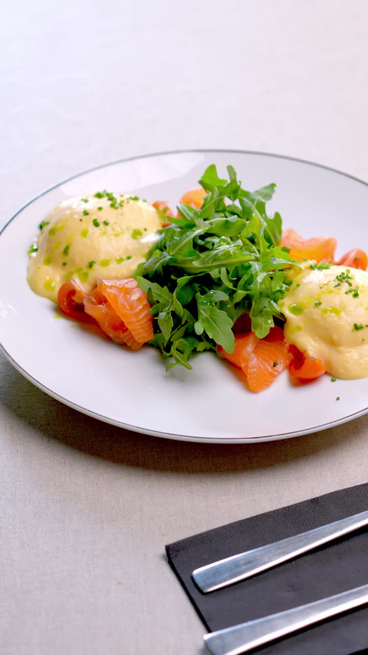 Poached eggs with hollandaise sauce are served alongside smoked salmon and fresh arugula, creating a visually appealing and nutritious breakfast option