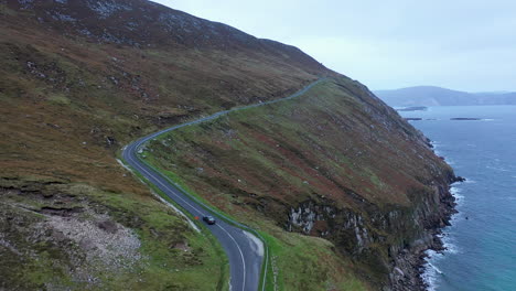 Cinematic-drone-shot-of-a-car-driving-near-Keem-Beach,-Ireland-on-the-Wild-Atlantic-Way