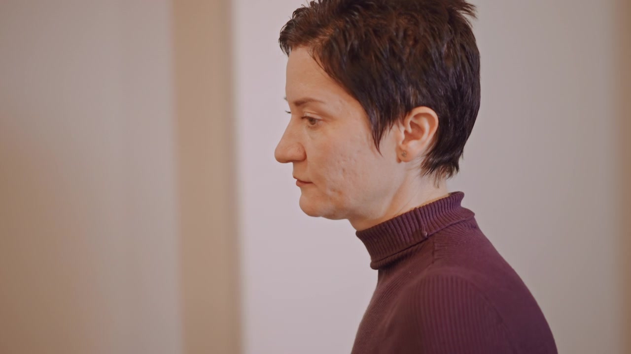 Vocal coach donna caucasica in studio di prova. Espressione concentrata mentre guida lo studente attraverso esercizi di respirazione, illuminazione soffusa, atmosfera di lezione intima, microfono e lavagna visibili.