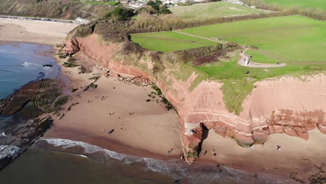 Aerial-Over-Orcombe-Point-And-Cliffs-In-Exmouth-With-Visitors-On-Beach-On-Sunny-Day