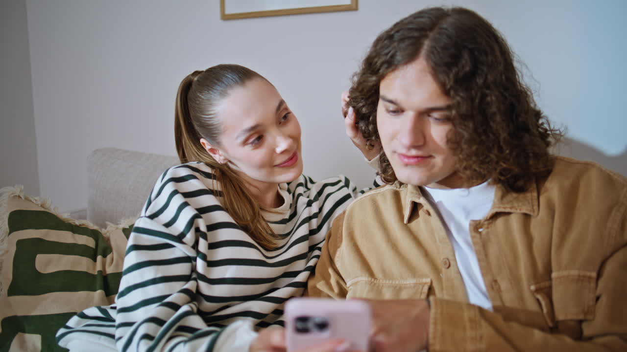 Romantic couple sharing smartphone watching social media content at sofa closeup