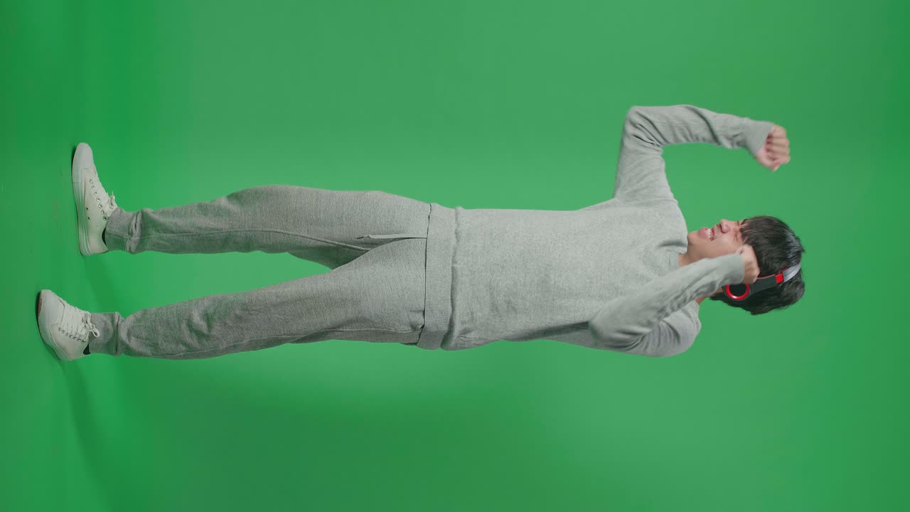Full Body Of Side View Asian Man Listening To Music With Headphones And Dancing In The Green Screen Studio