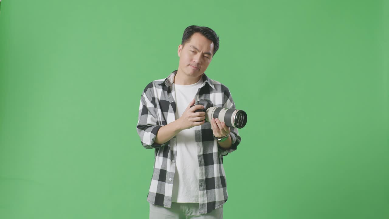 아시아 의 사진작가 가 손 에 카메라 를 들고 스튜디오 에서 녹색 스크린 배경 에 서 있는 동안 손 을 멈추는 표시 를 하고 있다