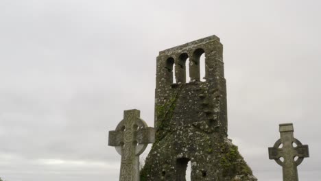 push in past rounded cross stone headstones of graveyard with moss covered brick wall tower of old church