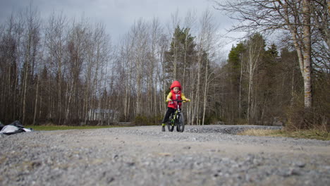 Young-child-boy-riding-bicycle-on-gravel-road-in-rural-area,-camera-follow