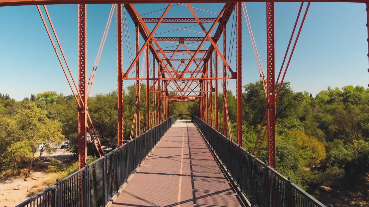Aerial drone view flying backwards through the Fair Oaks Bridge surrounded by green trees in California