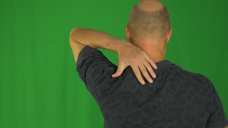 man rubbing his shoulders with left hand. back view waist up in polo shirt.