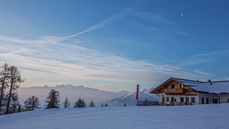 Tiro-De-Lapso-De-Tiempo-De-Hermoso-Amanecer-En-La-Cima-De-Las-Montañas-Nevadas-En-La-Mañana---Cabaña-De-Madera-Con-Ondeando-La-Bandera-Austriaca---Alpes,-Austria