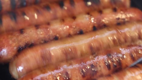primer plano de salchichas cocinándose uniformemente en una parrilla