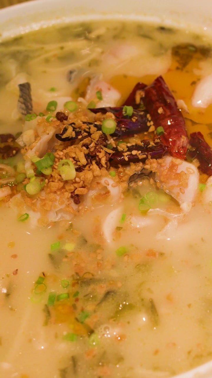 Nærbillede af dampende krydret fiskesuppe toppet med tørrede chilier og forårsløg.