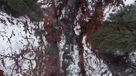 Toma-Aérea-De-Arriba-Hacia-Abajo-Que-Vuela-Hacia-Atrás-De-Un-Arroyo-En-El-Valle-Cubierto-De-Nieve-Durante-Los-Inviernos-En-Manali,-Himachal-Pradesh,-Filmada-Con-Un-Dron-En-4k