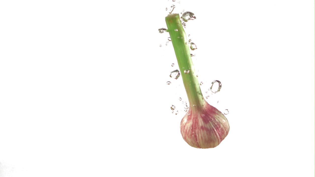 Bulbo d'aglio fresco che cade nell'acqua con bolle.