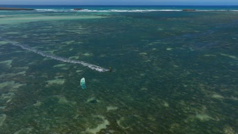 aerial view as drone follows a kitesurfer above reef waters. it overtakes the rider while tracking movement over the turquoise sea