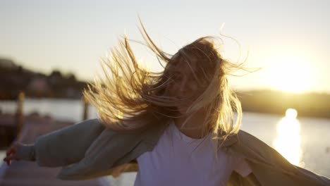 Close-up-footage-of-a-happy-girl-spinning-around-on-seaside-bridge,-blurred-background