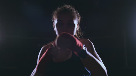 looking into the camera a beautiful female boxer strikes against a dark background with a backlit light. steadicam shot