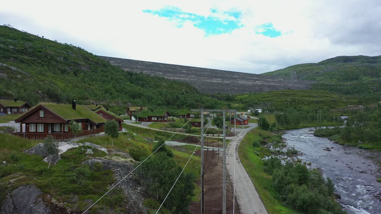 High voltage electrical cables  beside river with massive water reservoir sysen dam in background - Static aerial hovering above high voltage cables at Hardangervidda Norway