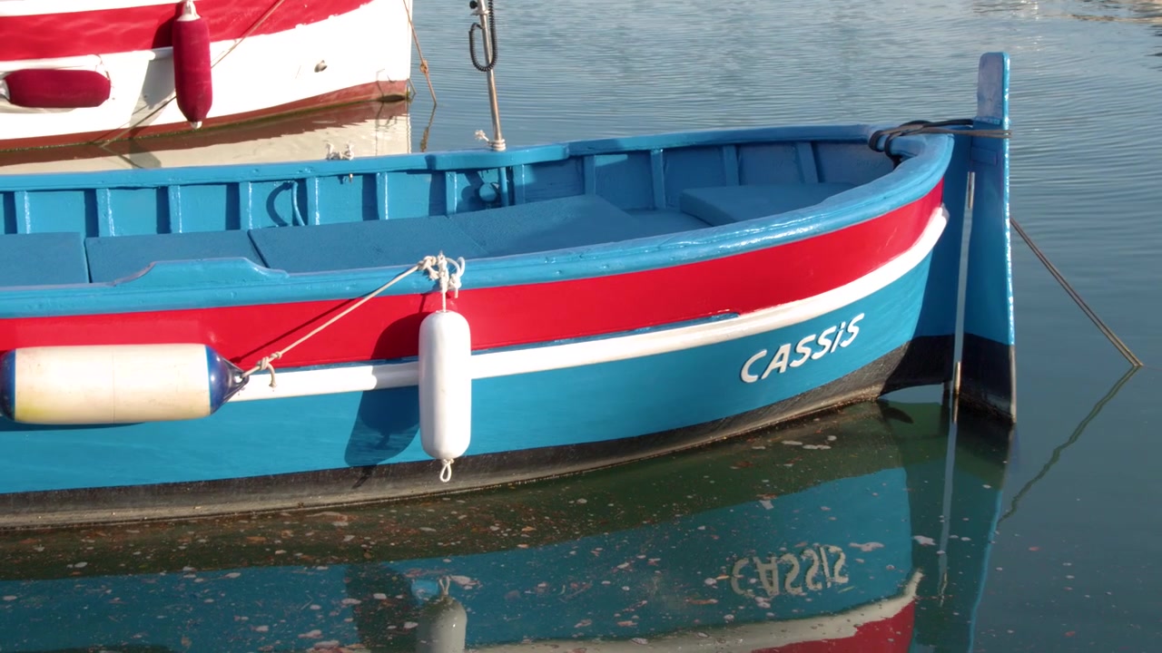 Inquadratura media statica di una colorata barca in legno tipo pointu che galleggia su acque calme del Mediterraneo.