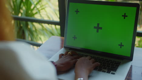Woman-from-bahind-typing-on-laptop-with-green-screen-on-table