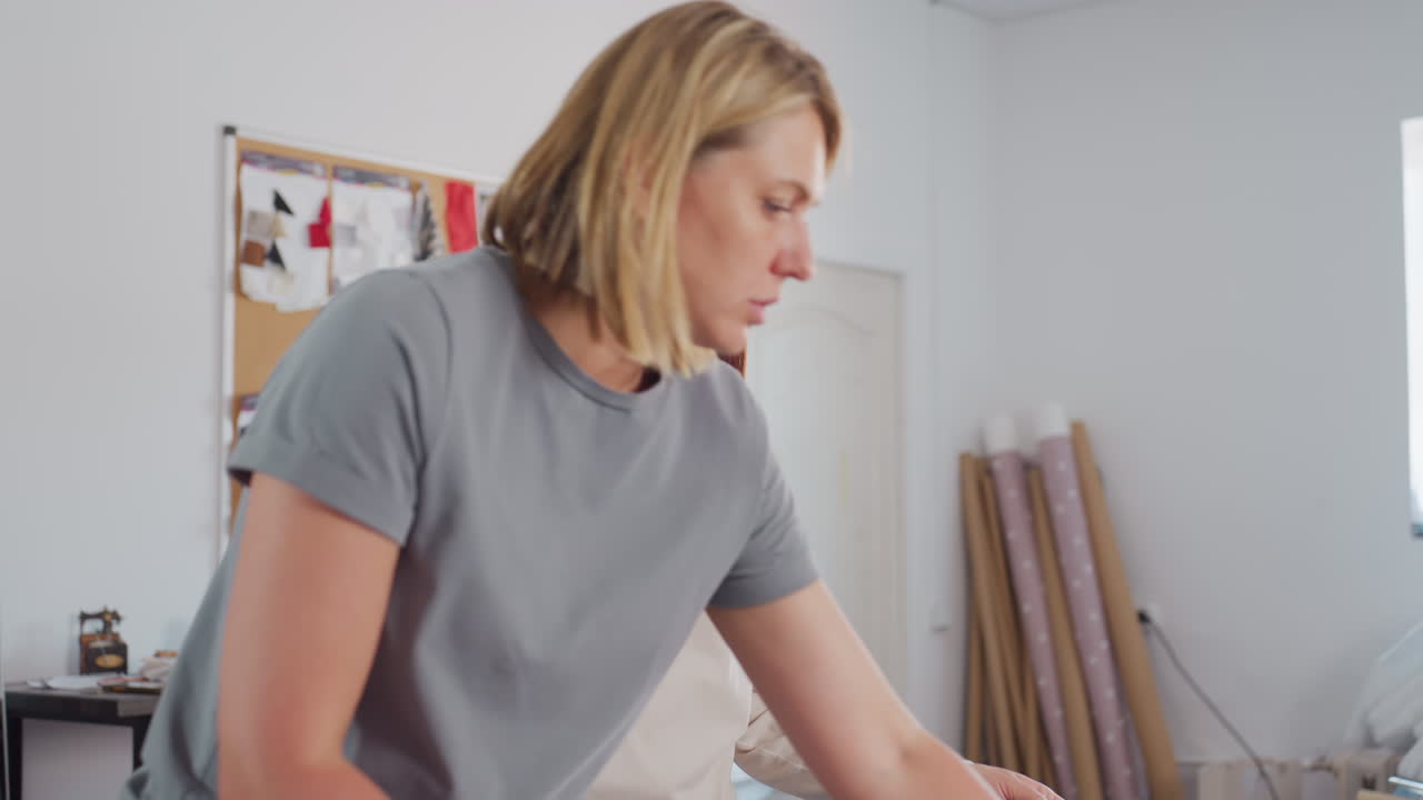 Elegant ladies walk together to examine fabric in bright creative workspace, focusing attention on details of color and texture, discussing design possibilities with concentration in relaxed setting