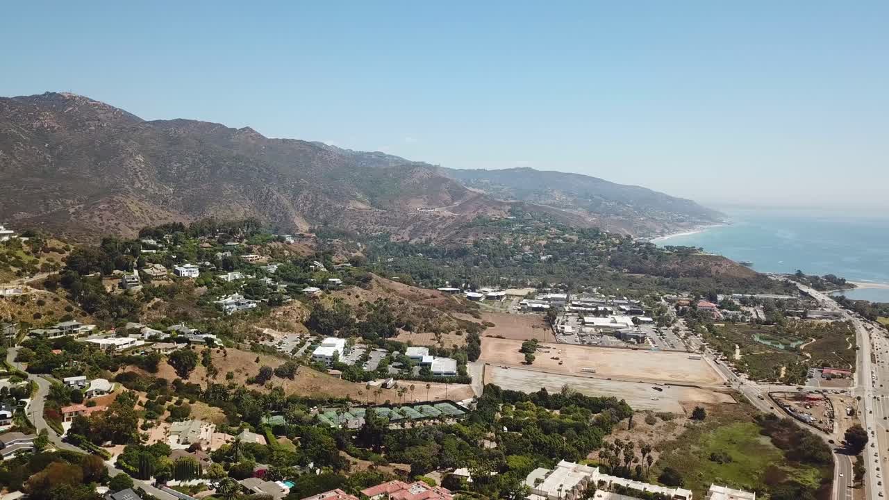 Aerial wide shot of Malibu Town with villas and mansion during sunny day. Ocean landscape with traffic on highway. California, America.