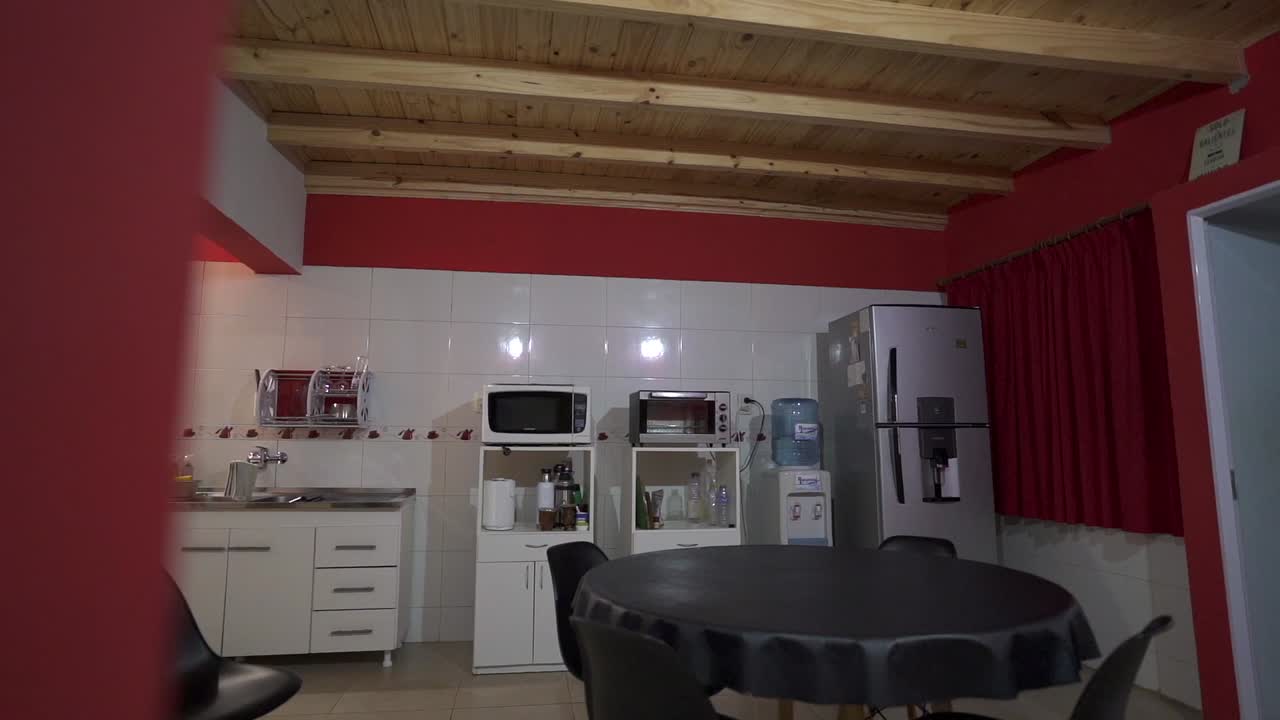 Slow panning camera clip showing red and white rustic Airbnb house kitchen, with wooden ceiling, large black dinning table, and black chairs.