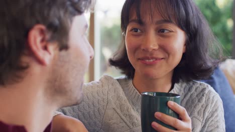 Video-of-back-view-of-happy-diverse-couple-sitting-on-sofa-and-drinking-coffee