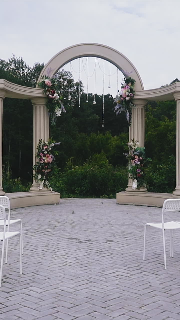 Slow motion: stylish modern wedding venue with rows of empty chairs and beautiful antique arch and columns near green trees on cloudy spring day