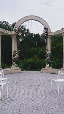 slow motion: stylish modern wedding venue with rows of empty chairs and beautiful antique arch and columns near green trees on cloudy spring day
