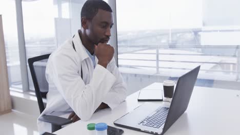African-american-male-doctor-using-laptop-in-hospital-office,-slow-motion