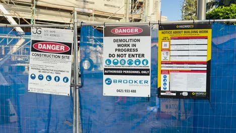 warning signs on a construction site fence in bright daylight, indicating demolition work and restricted access