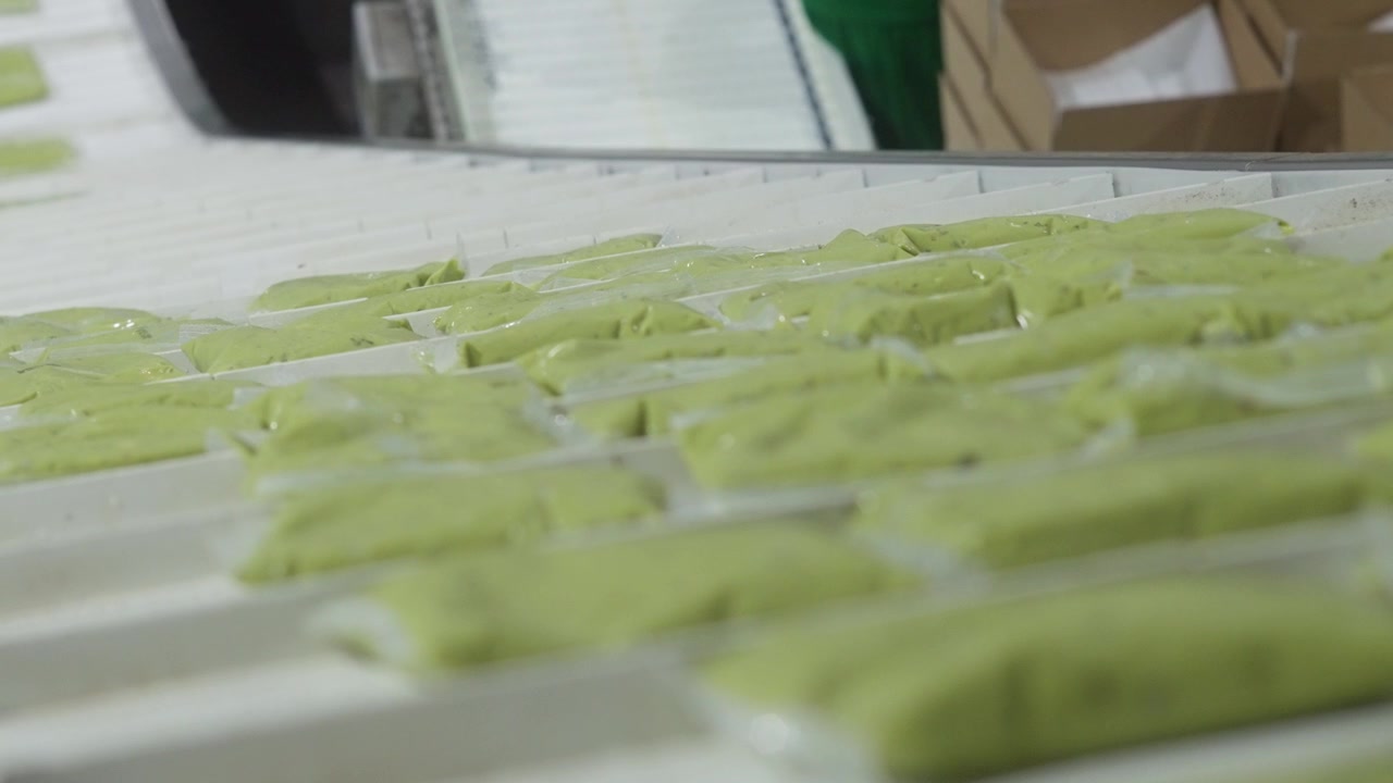 Filled guacamole trays aligned on conveyor belt ready for packaging in production facility