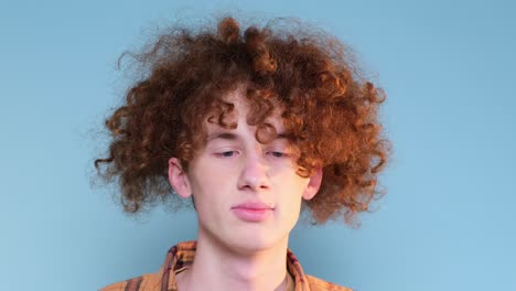 sad teenager on a blue background has red curly hair sad teenager on a blue background has red curly hair the boy is tired from studying and needs rest
