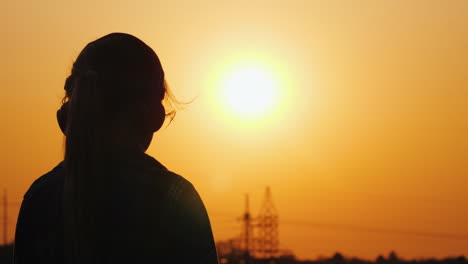 silueta de una chica con auriculares escuchando música con el telón de fondo de una gran puesta de sol y