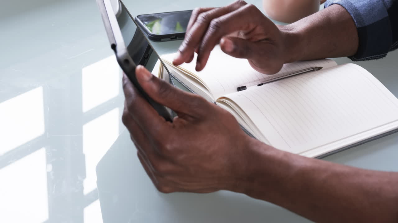 Usando tablet e taccuino, un uomo che lavora a casa con lo smartphone nelle vicinanze.