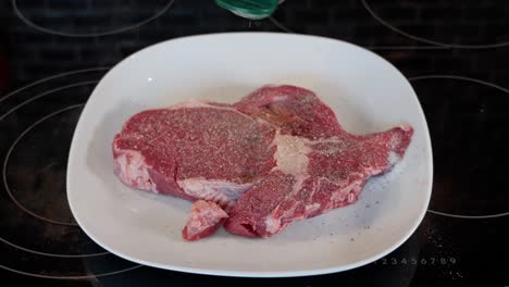 entrecote crudo en un plato blanco siendo sazonado con pimienta en la parte superior