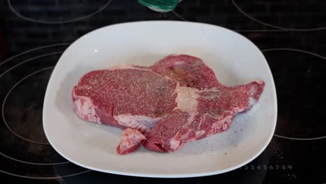 raw entrecote on a white plate being seasoned with pepper on top