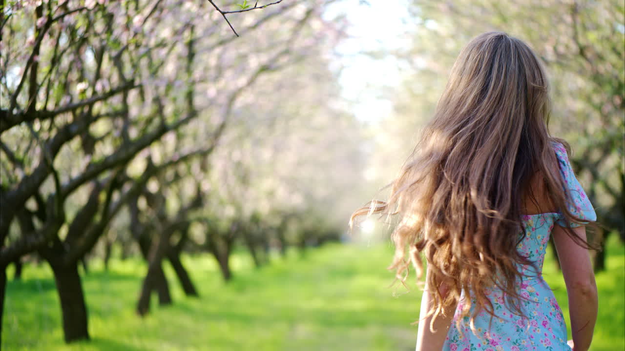 Donna bruna con un vestito blu che si gode un campo di mandorli in fiore