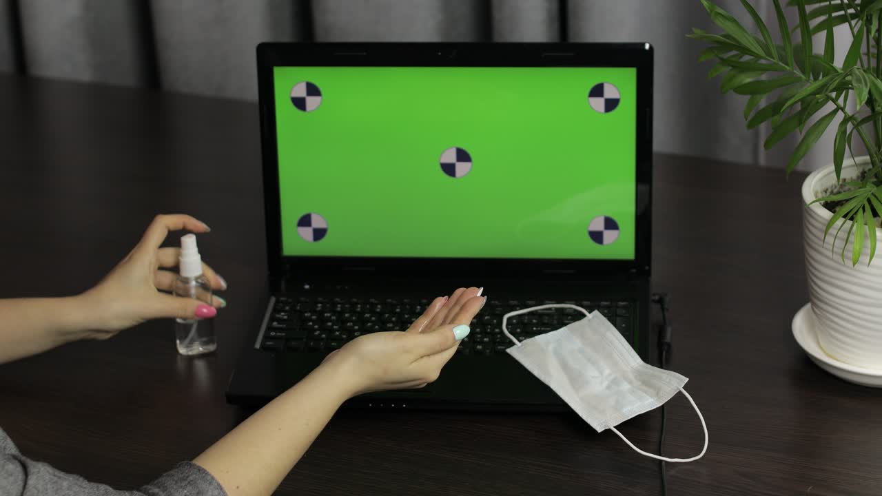 las manos de la mujer usan desinfectante cerca de la computadora portátil con pantalla verde. coronavirus