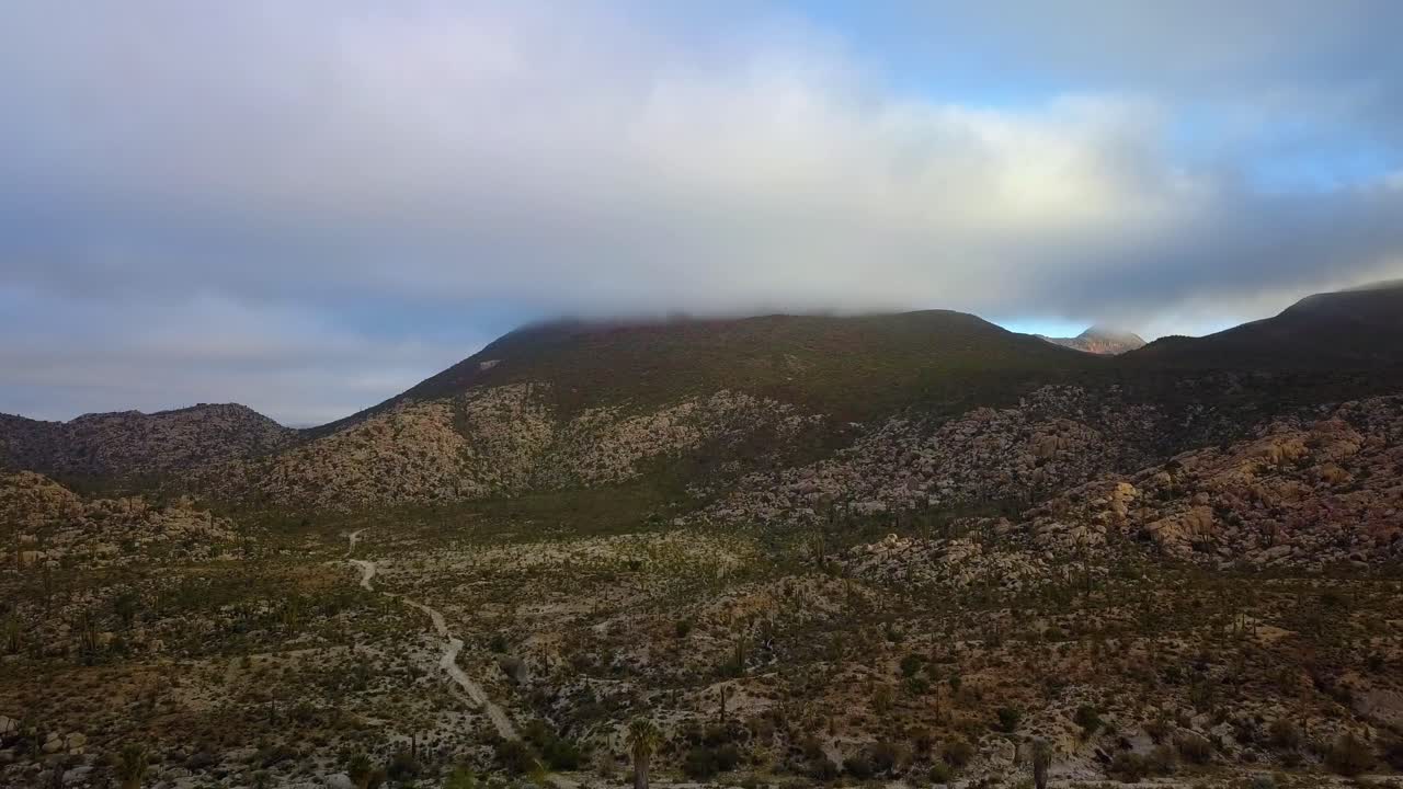 vista aérea sobre un desierto hacia una montaña cubierta de nubes, día parcialmente soleado, en catavina, méxico - dolly, tiro de drones