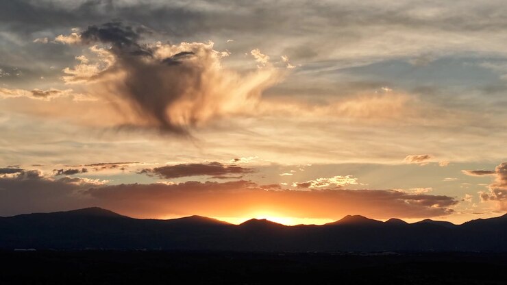 Timelapse con drone 4K UHD: cielo arancione intenso dopo il tramonto e scure sagome di montagne. L'ampio orizzonte cattura nuvole di pioggia alla deriva e cambiamenti climatici dinamici per sfondi di paesaggi naturali