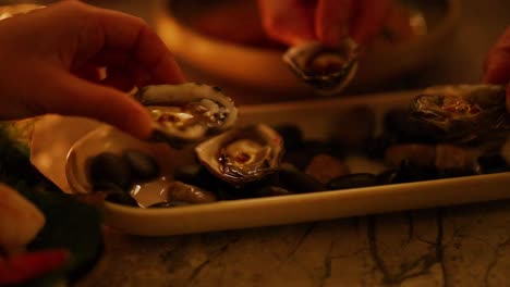 hands delicately handle oysters on a platter in warm, intimate candlelight, creating a cozy, inviting atmosphere