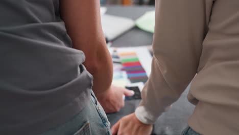back view of two fashion designers leaning over worktable, selecting colors from fabric samples, focusing on creative collaboration, decision making, teamwork, material choice, and design planning