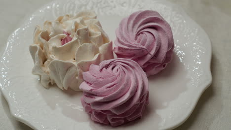 close up display of decorative white and pink cupcakes arranged on elegant white ceramic plate with delicate patterns, showing swirled icing design on light tablecloth in cozy setting
