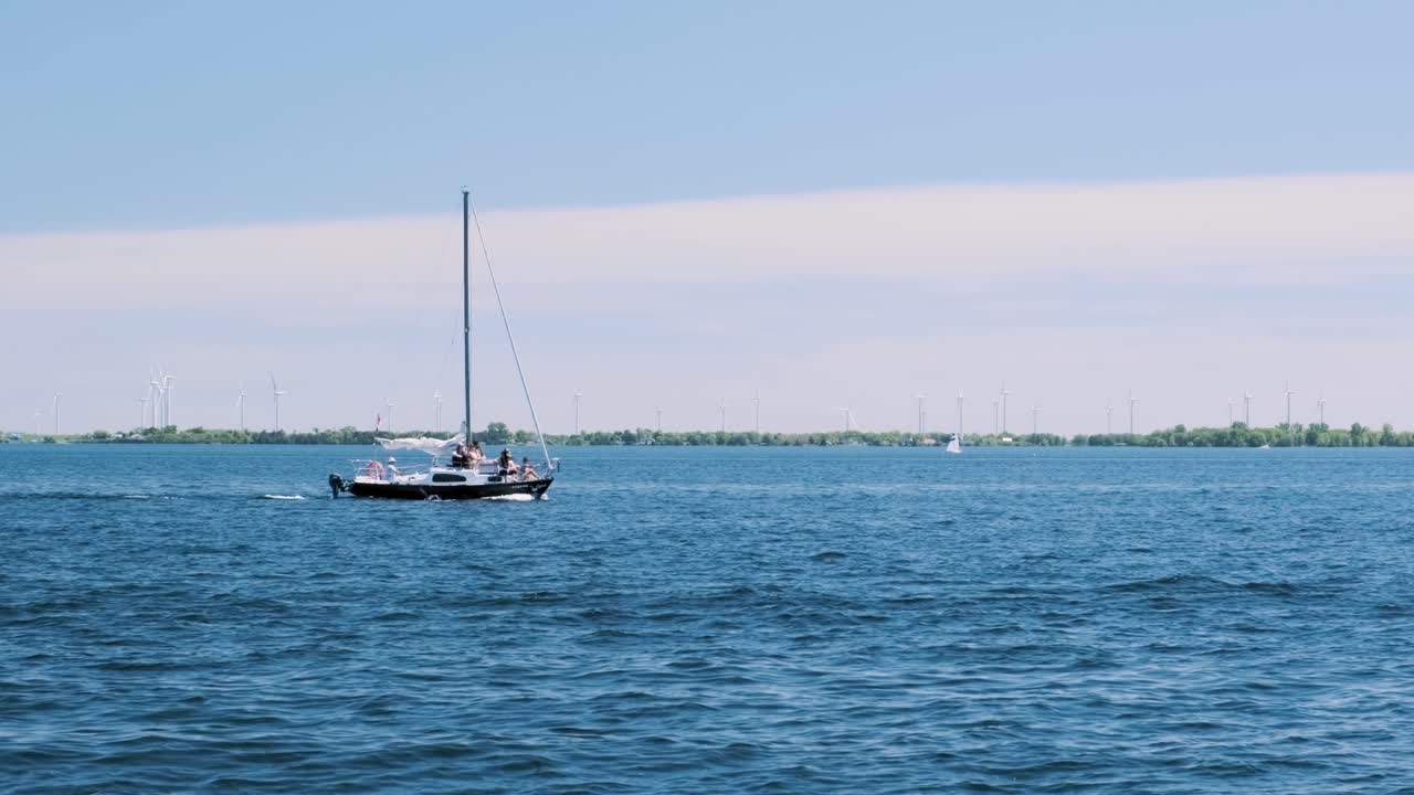 Slow motion shot of a small yacht floating through a bay with wind turbines spinning in the background