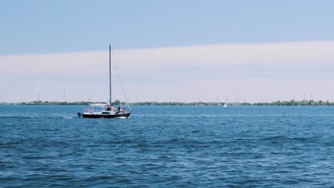 slow motion shot of a small yacht floating through a bay with wind turbines spinning in the background