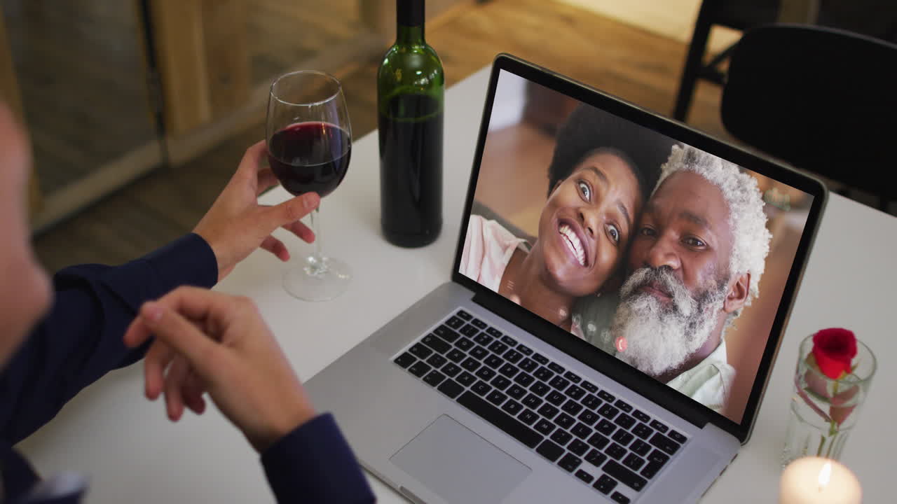 sección media de una mujer afroamericana bebiendo vino mientras hace una videollamada en una computadora portátil en casa